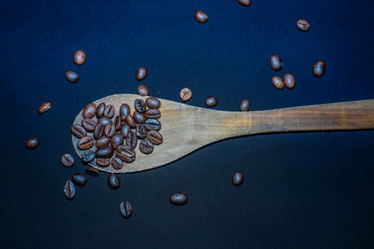 Black coffee beans are seen close up with a wooden spoon on a black cloth. photo