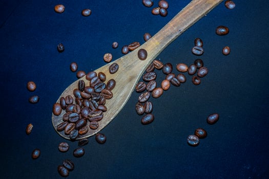 Black coffee beans are seen close up with a wooden spoon on a black cloth. photo