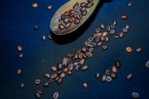 Black coffee beans are seen close up with a wooden spoon on a black cloth. photo
