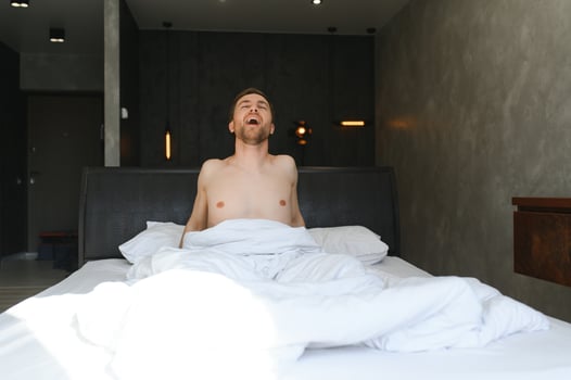 Young man waking up and rise hands stretching on white bed in the morning with sunlight through window photo