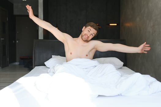 Young man sleeping waking up and stretching in his bed photo