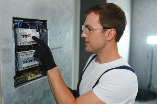 A male electrician works in a switchboard with an electrical connecting cable photo