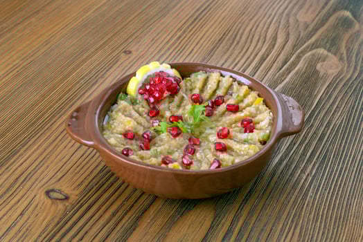 mutabal with pomegranate seeds and lemon slice served in dish isolated on table side view of arabic food photo