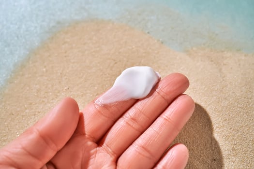 A smear of white cream with SPF on the fingers against a background of sand. photo