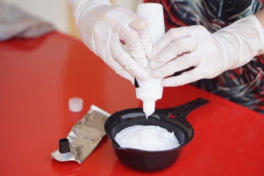 Close up hands wears gloves, squeezes dye hair color cream from tube in mix in black bowl before dying client's hair. Concept, hair beauty product for changing hair color by professional hairdresser. photo