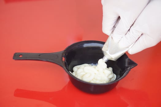 Close up hands wears gloves, squeezes dye hair color cream from tube in mix in black bowl before dying client's hair. Concept, hair beauty product for changing hair color by professional hairdresser. photo