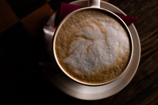 Closeup of the cup of cappuccino on the white plate on the dark wooden table. White cup of hot coffee latte  Top view. Copy Space. photo