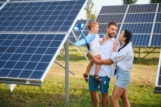 A wide shot of a happy family standing together and smiling at camera with a large solar panel in background photo