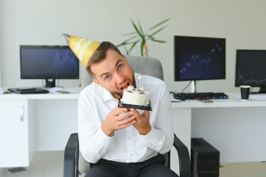 Young happy businessman celebrating his birthday in the office. He holds a cake in his hands. photo