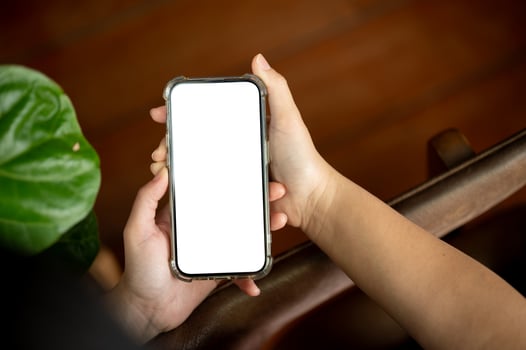 A woman holding a white-screen smartphone mockup over a blurred rustic wood background. photo