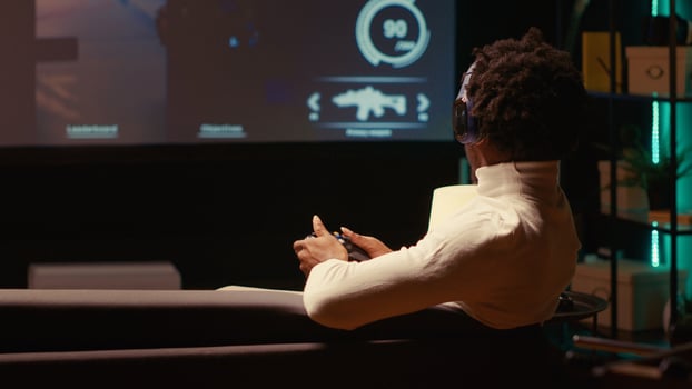 Man plays first person shooter videogame on smart TV with gun shooting at enemies in dark atmospheric setting. Gamer enjoying PvP online multiplayer game with players competing against each other photo