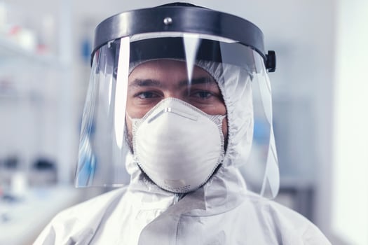 Tired healthcare scientist loooking at camera wearing ppe suit with face shieldin lab. Overworked researcher dressed in protective suit against invection with coronavirus during global epidemic. photo