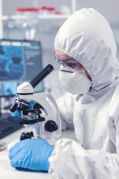Close up of chief researcher scientist adjusts microscope in time of coronavirus experiment. Virolog in coverall during coronavirus outbreak conducting healthcare scientific analysis. photo
