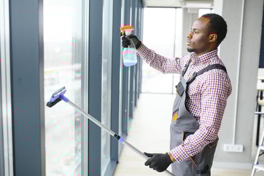 African Male professional cleaning service worker in overalls cleans the windows and shop windows of a store with special equipment photo