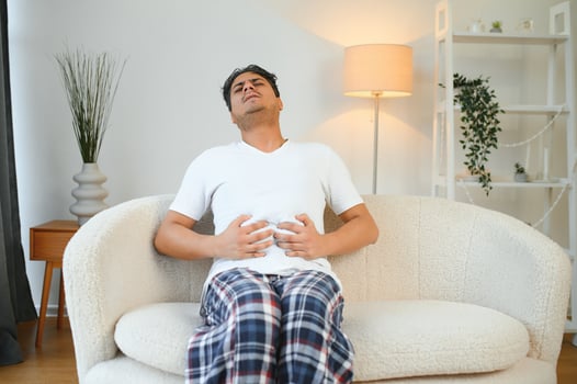 Sad exhausted guy of indian and arabian ethnicity, holds his hands on his stomach, grimaces from pain in his stomach, suffers from poisoning, spasm, stomach problems photo