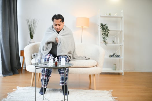 health, cold and people concept - sick young indian man in blanket having headache or fever at home photo