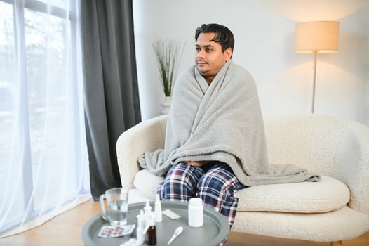 health, cold and people concept - sick young indian man in blanket having headache or fever at home photo