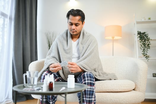 health, cold and people concept - sick young indian man in blanket having headache or fever at home photo