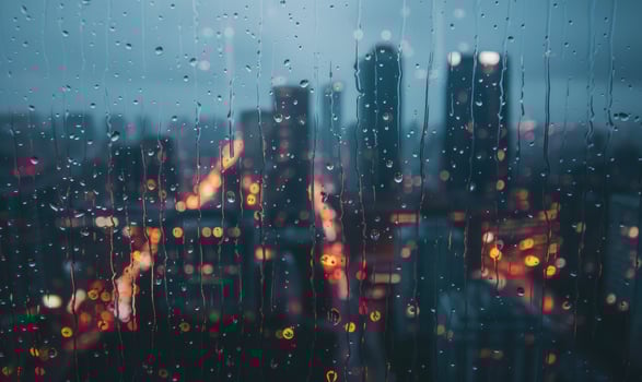 Raindrops streaking down a windowpane with a blurred cityscape in the background photo