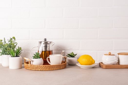 Beautiful kitchen background with glass teapot of fragrant tea, cup, lemon on wicker tray. Front view. White brick wall. A copy space. photo