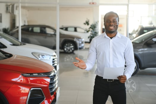 Cars Dealership Concept. Auto Seller Afro Man Standing In Automobile Center photo