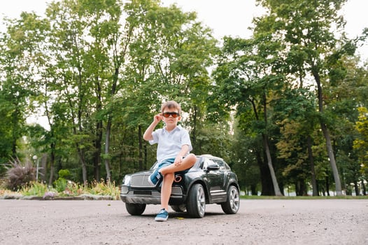 Cute boy in riding a black electric car in the park. Funny boy rides on a toy electric car. Copy space. photo