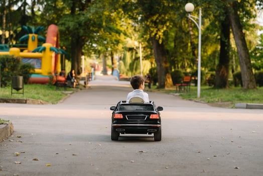 Cute boy in riding a black electric car in the park. Funny boy rides on a toy electric car. Copy space. photo