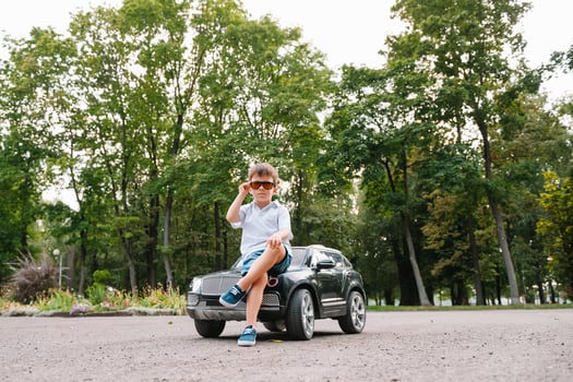 Cute boy in riding a black electric car in the park. Funny boy rides on a toy electric car. Copy space. photo