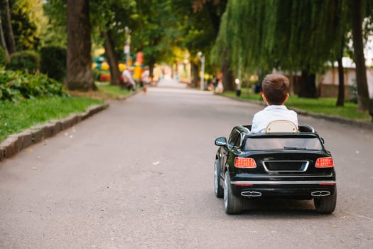 Cute boy in riding a black electric car in the park. Funny boy rides on a toy electric car. Copy space. photo
