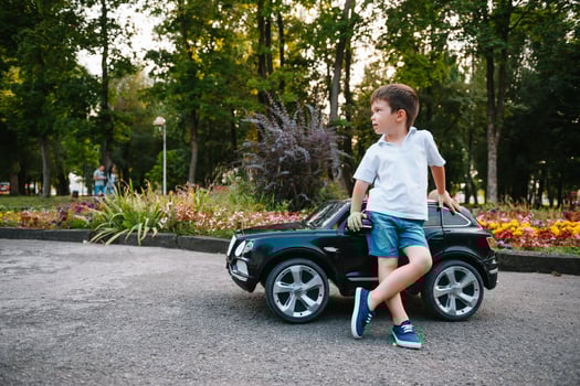 Cute boy in riding a black electric car in the park. Funny boy rides on a toy electric car. Copy space. photo