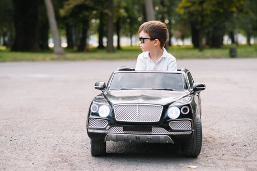 Cute boy in riding a black electric car in the park. Funny boy rides on a toy electric car. Copy space. photo