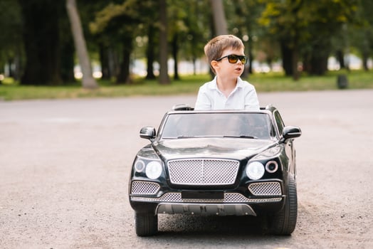 Cute boy in riding a black electric car in the park. Funny boy rides on a toy electric car. Copy space. photo
