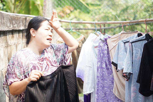 Asian woman housewife is working , drying cloth outdoor on sunny day. Feel hot. Concept, working or doing outdoor activity is risk to heat stroke symptom in hot weather condition.Global warming effect photo