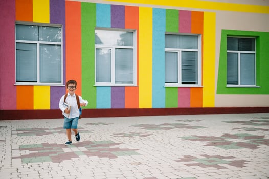 Back to school. Happy smiling boy in glasses is going to school for the first time. Child with backpack and book outdoors. Beginning of lessons. First day of fall. photo
