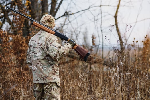 hunting, war, army and people concept - young soldier, ranger or hunter with gun walking in forest. photo