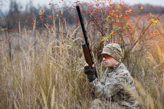 A male hunter with a gun while sitting takes aim at a forest. The concept of a successful hunt, an experienced hunter. Hunting the autumn season. The hunter has a rifle and a hunting uniform. photo