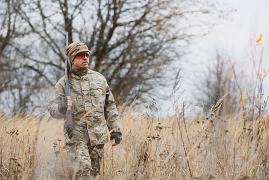 hunting, war, army and people concept - young soldier, ranger or hunter with gun walking in forest. photo