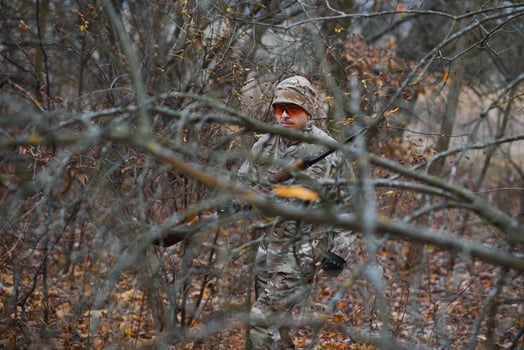 hunting, war, army and people concept - young soldier, ranger or hunter with gun walking in forest photo