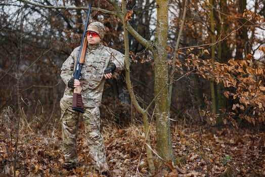 hunting, war, army and people concept - young soldier, ranger or hunter with gun walking in forest photo