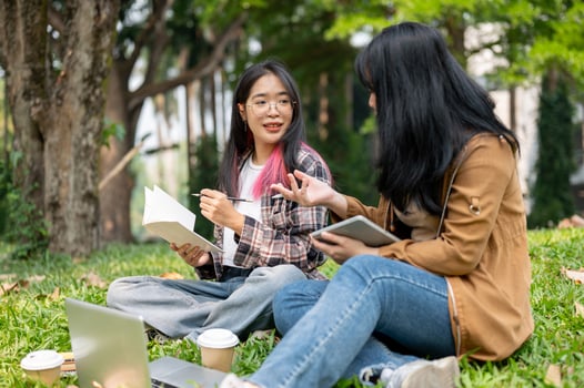 Two young Asian female students are sitting on the grass in a park, studying together. photo