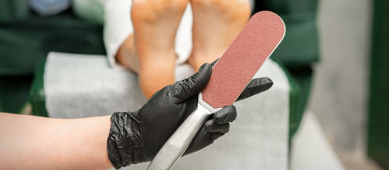 Special grater for scrubbing heels in hands of nail pedicure technician on feet background in beauty salon closeup. photo
