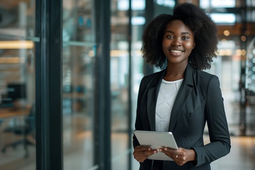 A young black woman in a business suit holding a tablet stands amidst the glass partitions of the office photo