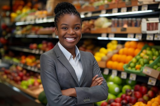 young black woman wearing a gray suit is smiling with her arms folded across her chest standing in her own fruit store photo