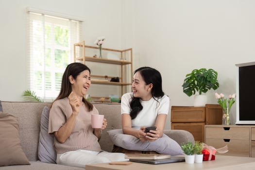 Happy senior mother with adult daughter sitting on couch and holding cups with coffee or tea at home. Enjoy family concept photo
