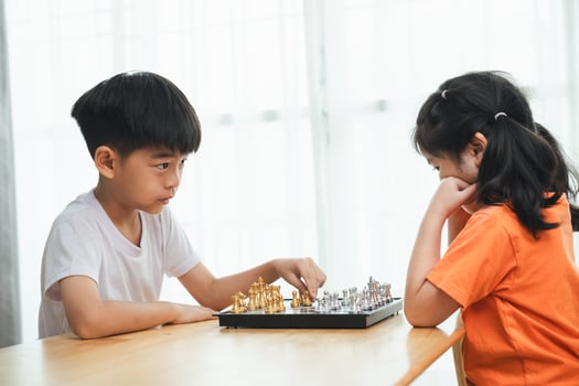 Two children playing a game of chess. One is wearing a white shirt and the other is wearing an orange shirt photo