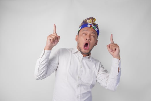 Surprised Balinese man wearing traditional headdress called udeng pointing up to the copy space upwards over isolated white background photo