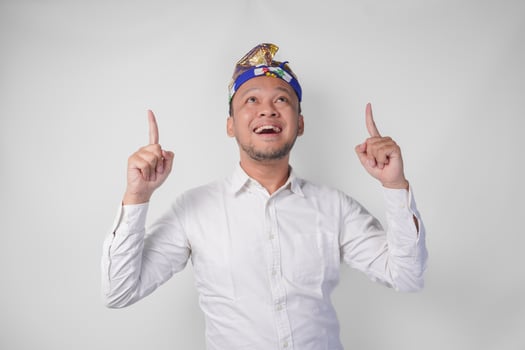 Surprised Balinese man wearing traditional headdress called udeng pointing up to the copy space upwards over isolated white background photo