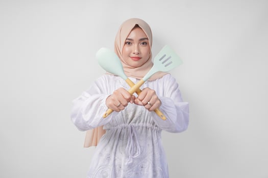 Displeased Asian woman in veil hijab doing a refusal or rejection sign, saying no, asking to stop gesture using spatula and cooking utensils photo