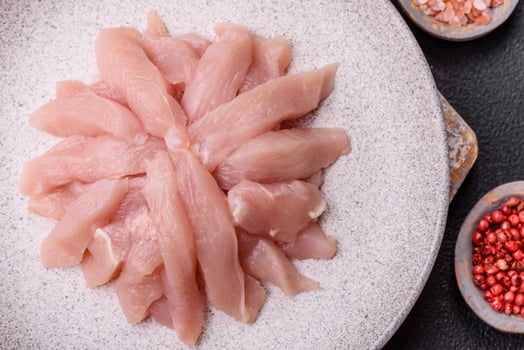 Slices of raw chicken or turkey fillet with salt, spices and herbs photo