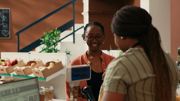 Local vendor weighting bulk products on sale for female buyer, small business owner at neighborhood grocery store. African american woman selling pasta and sauces in reusable glass jars. photo